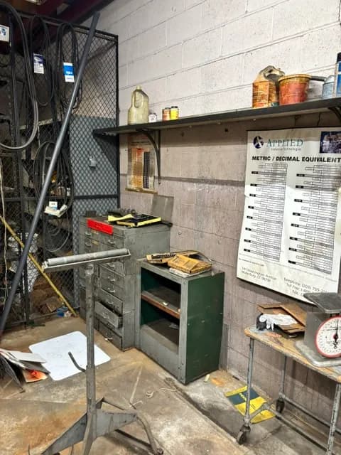 A workshop corner with a tool cabinet, wall chart, and hanging scale.