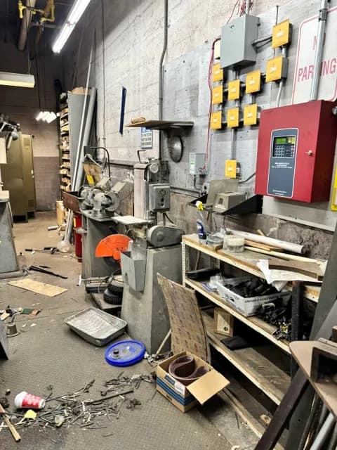 A workshop with a drill press, fire-alarm panel, and electrical panels.