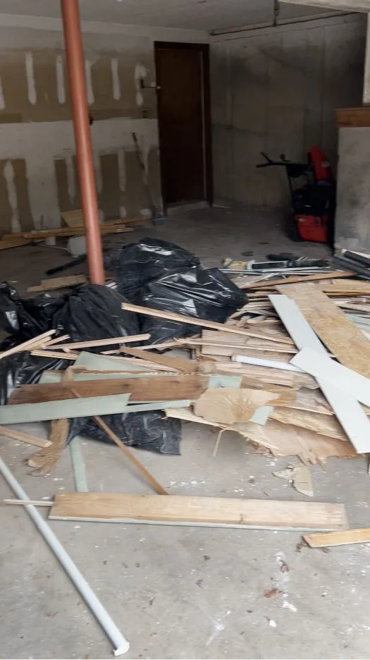 A basement filled with demolition debris, lumber, and contractor bags.